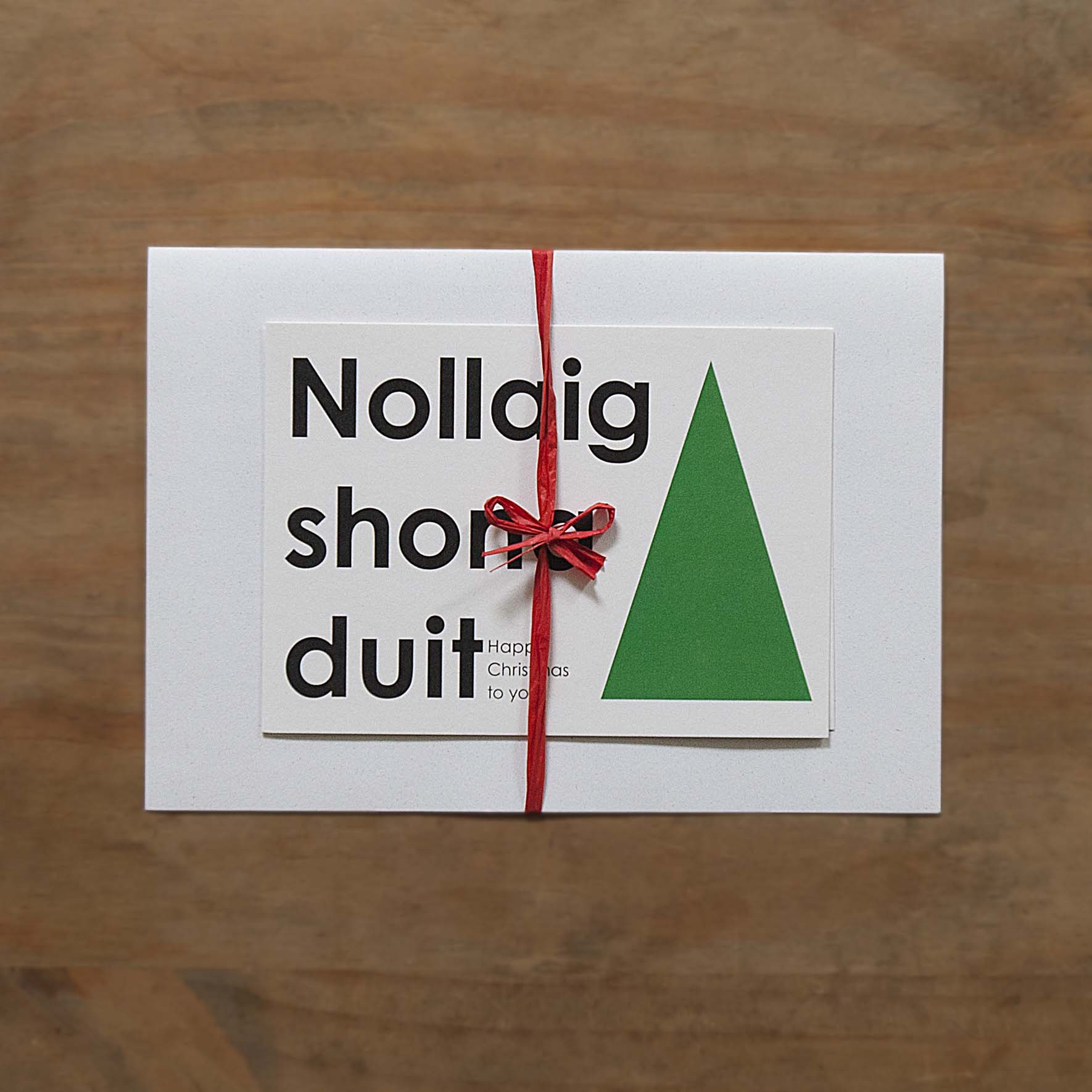 the photograph shows a folded letter, with which a christmas card is tied on with a red raffia, lying on a wooden desk.