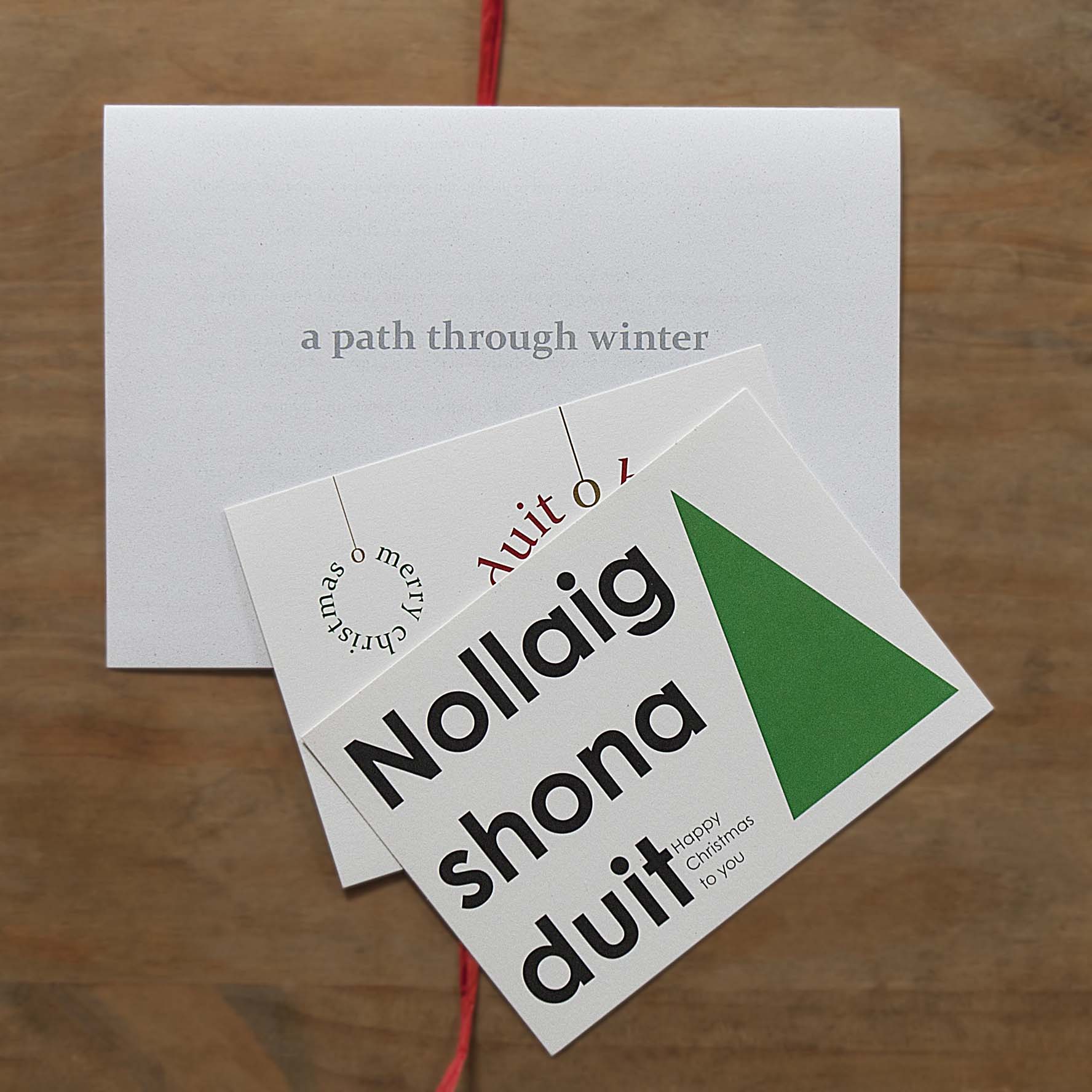 the photograph shows a folded letter in the top left, on which is the headline 'a path though winter' in grey bold lower case letters, two christmas cards lying shifted over partly the letter and the wooden desk, and a red raffia underneath.