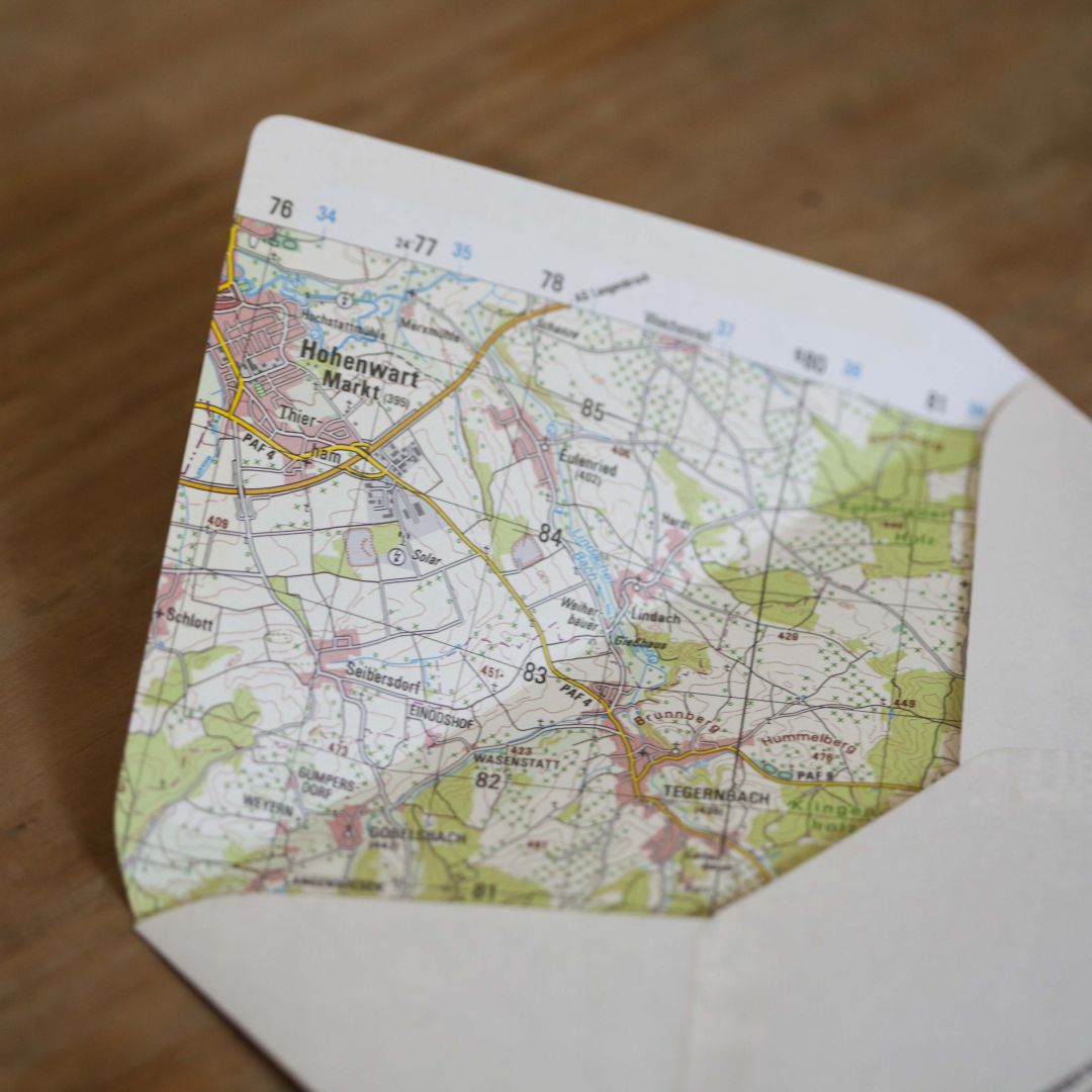 the photograph shows an envelope on a wooden desk. the inside of the envelope reveals it was made from an old map.